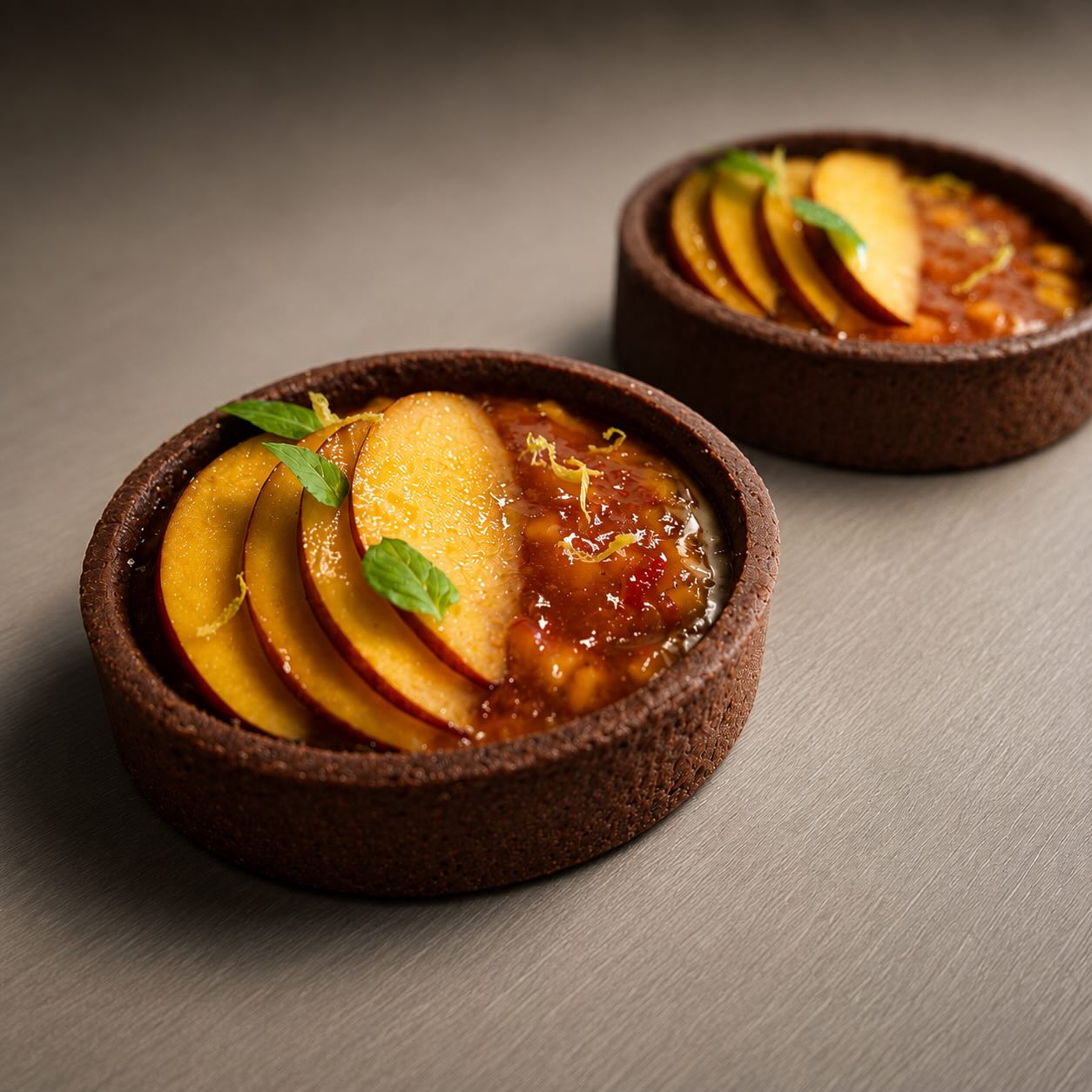 Chocolate tartlet topped with fresh peach slices, peach and basil compote and a basil leaf